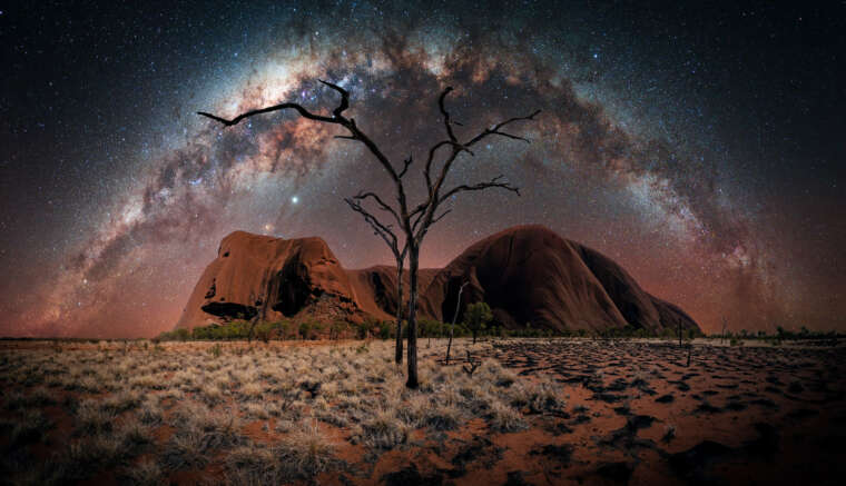 Uluru`s Night von Nacht- und Astrofotograf Stefan Liebermann - Night Panorama of the Uluru in Australia. In the foreground you can spot burned down trees and contrast between dry gras and burned down regions. In the sky is the milky way arch.