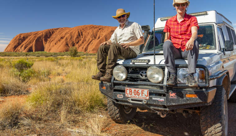 die Fotografen Aneta und Dirk Bleyer sitzen auf der Kühlerhaube eines Jeeps am Uluru in Australien