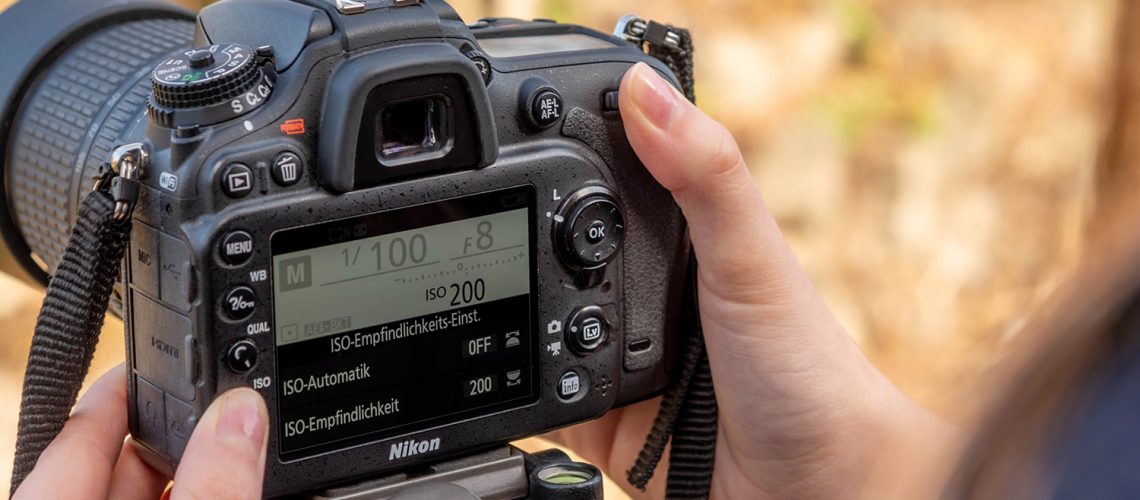 Eine Frau stellt den ISO-Wert an einer Nikon Spiegelreflexkamera über das Display auf ISO 200