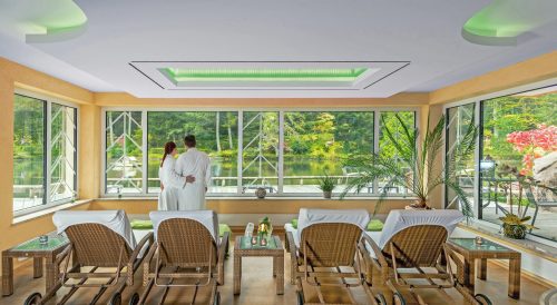 Ein Paar steht im Bademantel am Fenster des Wellnessbereichs im Hotel Langenwaldsee bei Freudenstadt und blickt auf den See